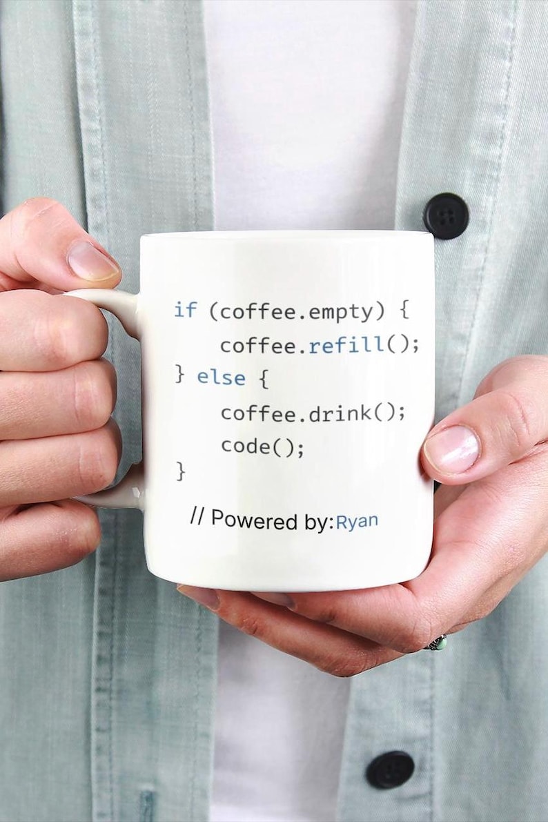 May include: White ceramic coffee mug with black text that reads "if (coffee.empty) { coffee.refill(); } else { coffee.drink(); code(); } // Powered by: Ryan". The mug has a handle and is held by a person.