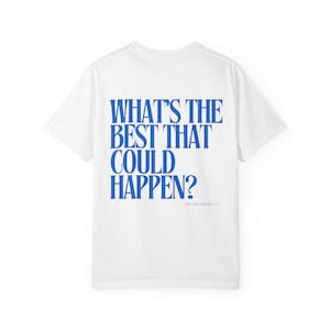 May include: White t-shirt with the blue text "WHAT'S THE BEST THAT COULD HAPPEN?" on the back. The shirt also has the text "BIG DREAMERS" in a smaller font. The shirt is made of a soft material.