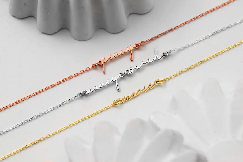 May include: Three delicate name necklaces in rose gold, silver, and gold. Each necklace features a cursive name: "Penny", "Nancy Sarah", and "Marie". The chains are fine and the names are elegantly scripted.