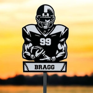 May include: Black and white silhouette of a football player wearing a helmet and holding a football. The player is wearing a jersey with the number 99 and the name "BRAGG" on a sign below.