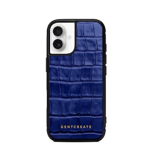 A crocodile-textured iPhone case. The case features a Glossy, reptile-inspired Glossy with raised scales that give it a luxurious, high-end look. The phone case has a black border, highlighting its sleek and modern design. The person's hand, with neatly manicured red nails, is seen against a backdrop of denim jeans, adding a stylish, fashionable touch to the image. The brand name "GENTCREATE" is subtly visible on the case.