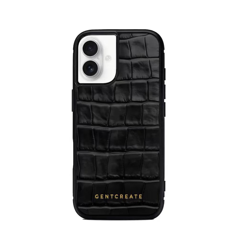 A crocodile-textured iPhone case. The case features a Glossy, reptile-inspired Glossy with raised scales that give it a luxurious, high-end look. The phone case has a black border, highlighting its sleek and modern design. The person's hand, with neatly manicured red nails, is seen against a backdrop of denim jeans, adding a stylish, fashionable touch to the image. The brand name "GENTCREATE" is subtly visible on the case.