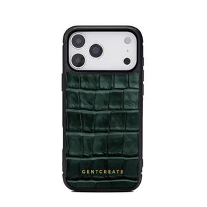 A crocodile-textured iPhone case. The case features a Glossy, reptile-inspired Glossy with raised scales that give it a luxurious, high-end look. The phone case has a black border, highlighting its sleek and modern design. The person's hand, with neatly manicured red nails, is seen against a backdrop of denim jeans, adding a stylish, fashionable touch to the image. The brand name "GENTCREATE" is subtly visible on the case.