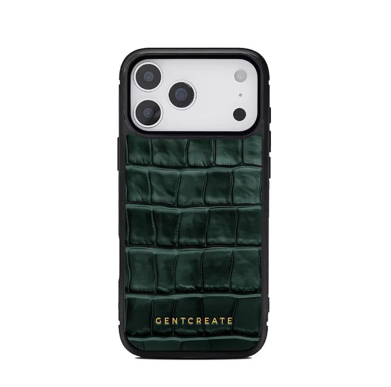 A crocodile-textured iPhone case. The case features a Glossy, reptile-inspired Glossy with raised scales that give it a luxurious, high-end look. The phone case has a black border, highlighting its sleek and modern design. The person's hand, with neatly manicured red nails, is seen against a backdrop of denim jeans, adding a stylish, fashionable touch to the image. The brand name "GENTCREATE" is subtly visible on the case.
