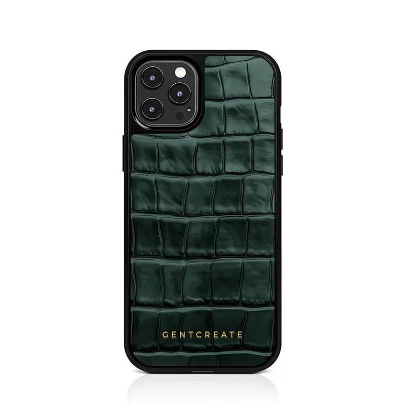 A crocodile-textured iPhone case. The case features a Glossy, reptile-inspired Glossy with raised scales that give it a luxurious, high-end look. The phone case has a black border, highlighting its sleek and modern design. The person's hand, with neatly manicured red nails, is seen against a backdrop of denim jeans, adding a stylish, fashionable touch to the image. The brand name "GENTCREATE" is subtly visible on the case.
