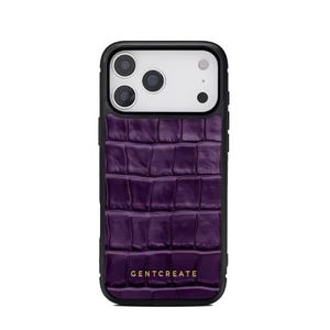 A crocodile-textured iPhone case. The case features a Glossy, reptile-inspired Glossy with raised scales that give it a luxurious, high-end look. The phone case has a black border, highlighting its sleek and modern design. The person's hand, with neatly manicured red nails, is seen against a backdrop of denim jeans, adding a stylish, fashionable touch to the image. The brand name "GENTCREATE" is subtly visible on the case.
