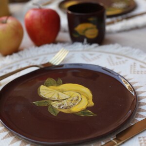 May include: A brown ceramic plate with a yellow lemon design. The plate is on a white table with a white and brown placemat.
