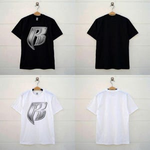 Könnte beinhalten: Schwarze und weiße T-Shirts mit einem metallisch silbernen Buchstaben "B"-Design. Die Shirts werden auf Kleiderbügeln präsentiert, die Vorder- und Rückseite zeigen. Die T-Shirts sind kurzärmelig.