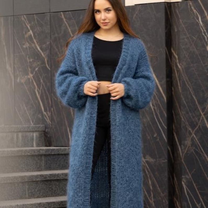 May include: A long, open-front cardigan in a dusty blue hue, featuring a fuzzy, textured knit construction, long sleeves with ribbed cuffs, and a ribbed trim along the front opening that extends down to the hemline, reaching below the knees.