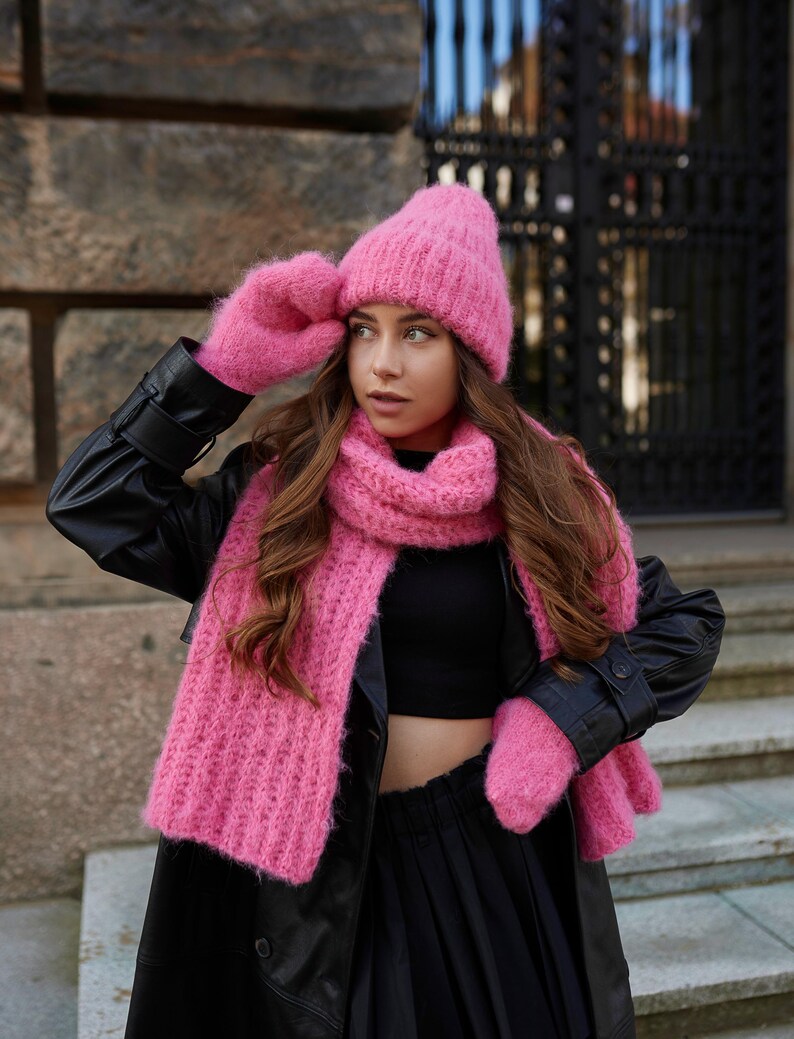 Puede incluir: Un gorro de punto rosa brillante, una bufanda larga de canal&eacute; a juego y un par de manoplas de punto a juego. El conjunto presenta una construcci&oacute;n de hilo difuso y texturizado en un tono rosa vibrante, ofreciendo un aspecto coherente.