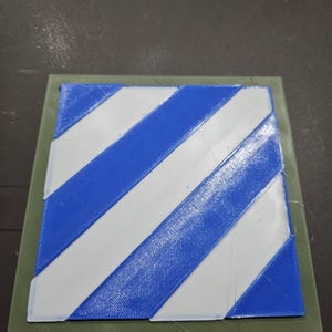 May include: A 3D-printed object featuring a blue and white striped pattern, set on a green square base. The diagonal stripes alternate in color, creating a visually striking design. The object is likely a decorative piece or a component for a larger project.
