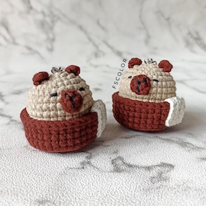 May include: Two handmade crochet bear ornaments. Each bear is beige with dark red accents for the nose, ears, and cup. The bears are sitting in a dark red cup with a white handle. The text "FSCOLOR" is visible on the right side.