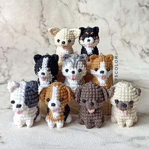 May include: A selection of crochet dog ornaments, each with a unique design and colour scheme. The dogs are crafted from yarn, with details in black, brown, and grey. They are arranged in a wooden box, showcasing their individual features.