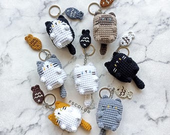 May include: A set of nine crocheted cat keychains with fish charms. The cats are in various colors, including white, gray, black, and brown. Each keychain has a metal ring for attaching to keys or bags.
