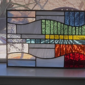 May include: A stained glass window panel with a geometric design featuring wavy lines in shades of blue, green, yellow, orange, and red.