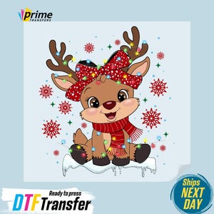 May include: A cartoon reindeer with a red bow, scarf, and string lights. The reindeer is brown with large eyes and is sitting on a snow-covered surface. Red snowflakes are scattered around the reindeer. The text "DTF Transfer" is at the bottom.