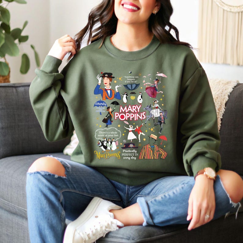 Puede incluir: Una sudadera verde oliva con un gr&aacute;fico colorido de personajes y citas de Mary Poppins. El dise&ntilde;o incluye ilustraciones de Mary Poppins, ping&uuml;inos y otros elementos de la pel&iacute;cula. Las palabras "MARY POPPINS" se muestran de forma destacada.
