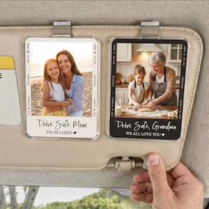 May include: Two rectangular car visor clips featuring photo inserts. The left clip shows a woman and child on a beach with text reading Drive Safe Mom FROM JAMES. The right clip shows a woman and child baking with text reading Drive Safe, Grandma WE ALL LOVE YOU.