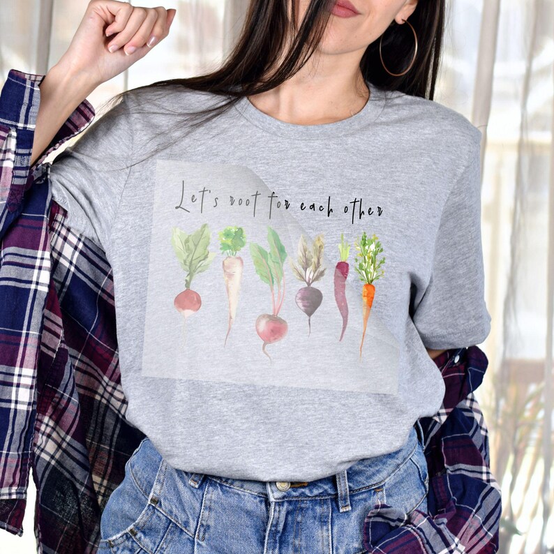 K&ouml;nnte beinhalten: Graues T-Shirt mit einer Aquarell-Illustration verschiedener Wurzelgem&uuml;se und dem Text "Let's root for each other".
