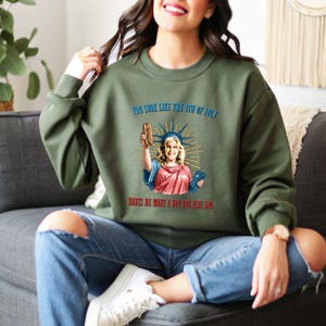 May include: Olive green sweatshirt with a graphic of a woman dressed as the Statue of Liberty holding a hot dog. The text on the sweatshirt reads "YOU LOOK LIKE THE 4TH OF JULY MAKES ME WANT A HOT DOG REAL BAD."
