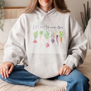 K&ouml;nnte beinhalten: Ein grauer Hoodie mit einer wei&szlig;en Grafik von Gem&uuml;se und dem Text "Let's root for each other".