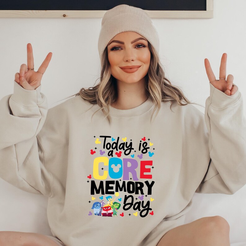 May include: A beige sweatshirt with the text "Today is a CORE MEMORY Day" in colorful letters. The text is surrounded by small Mickey Mouse heads and stars. There are five characters from the movie Inside Out on the bottom of the sweatshirt.