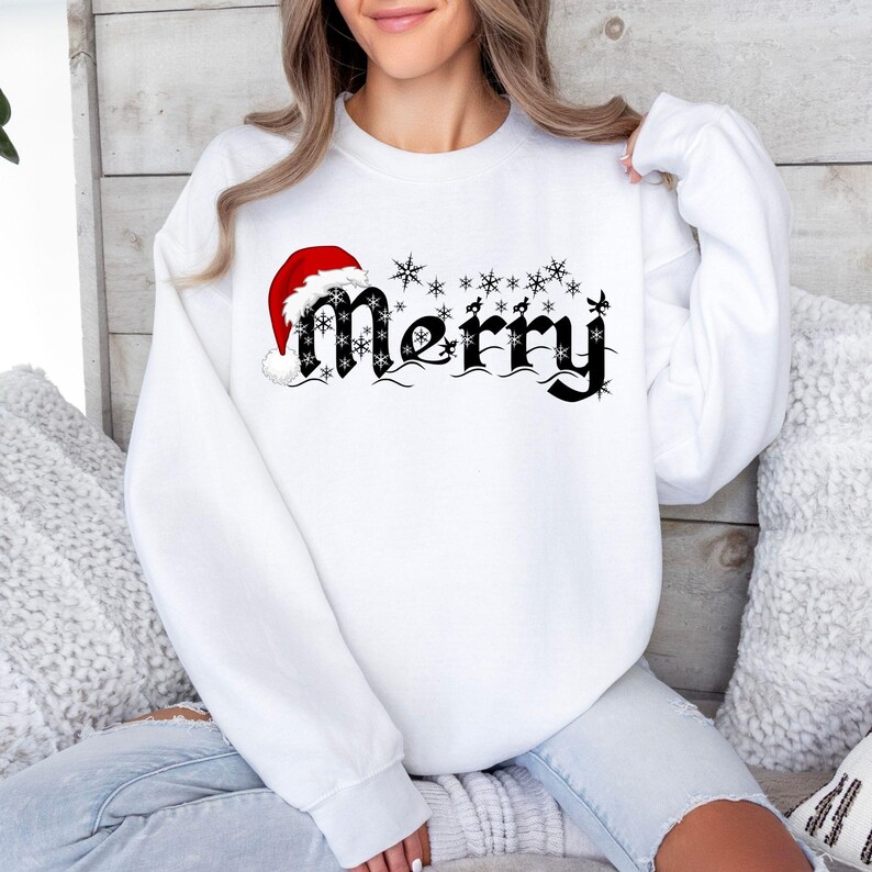 May include: White sweatshirt with the word "Merry" in black script, adorned with snowflakes and a Santa hat. The design is festive and suitable for the holiday season. The sweatshirt is a long-sleeved crew neck.