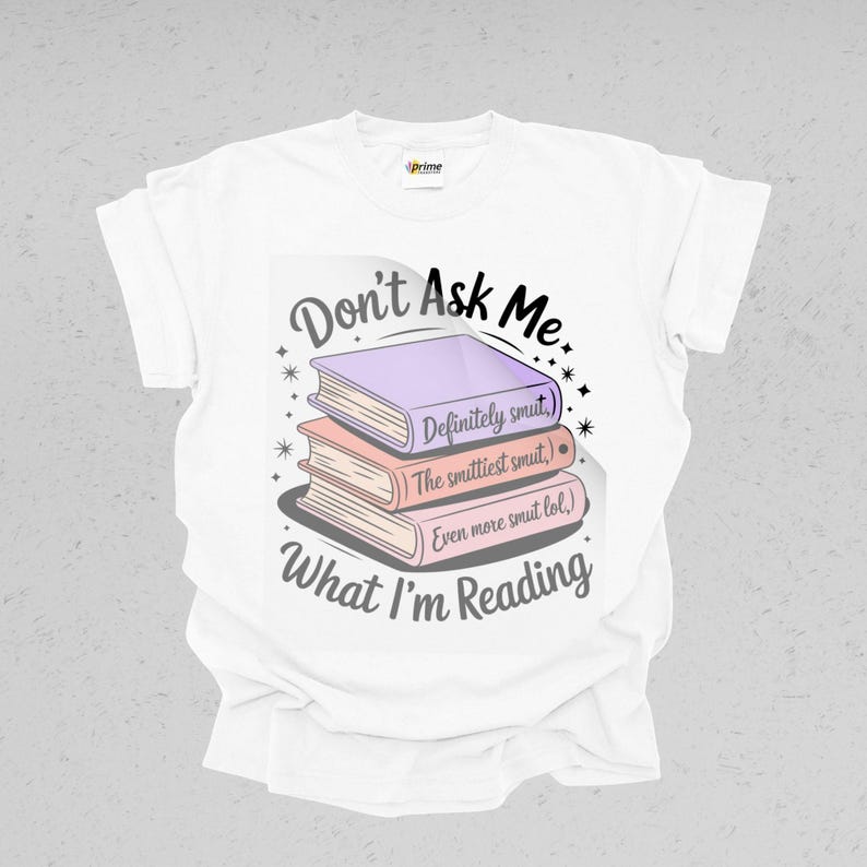 May include: White t-shirt featuring a graphic of three stacked books with the text "Don't Ask Me What I'm Reading." The books are labeled "Definitely smut," "The smuttiest smut," and "Even more smut lol."