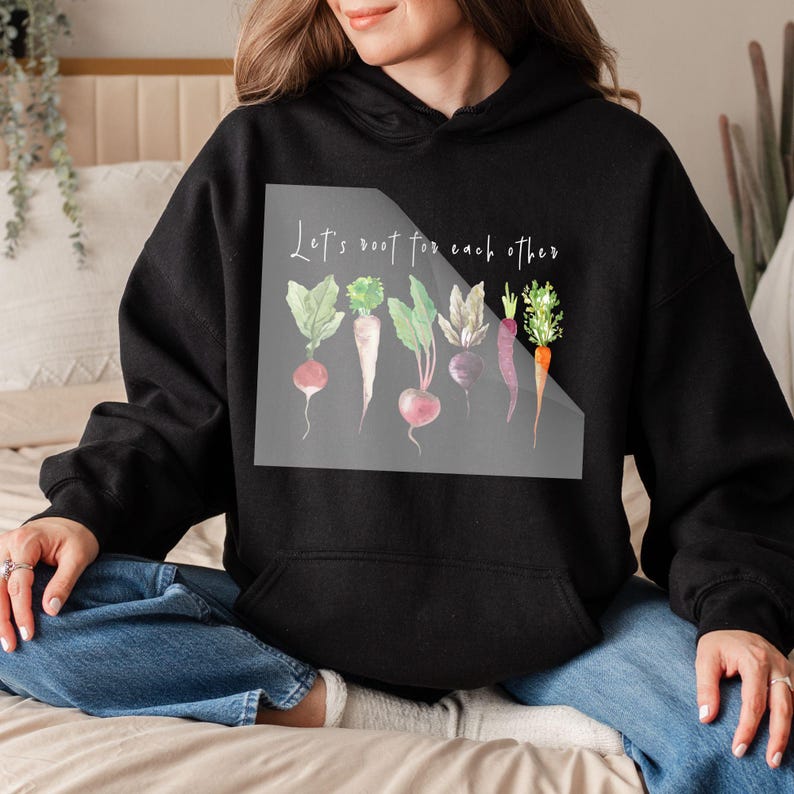 K&ouml;nnte beinhalten: Ein schwarzer Hoodie mit einer wei&szlig;en Grafik von Gem&uuml;se und dem Text "Let's root for each other".