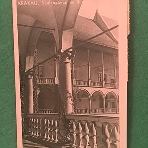 May include: Vintage black and white postcard featuring an architectural scene. The postcard shows a building with arched walkways, columns, and a balustrade. The text "KRAKAU. Säulengänge im Bur" is printed at the top.