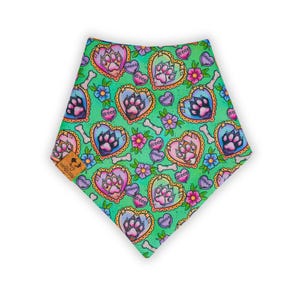 May include: A dog bandana with a repeating pattern of paw prints inside heart shapes, bones, and flowers on a green background. The hearts have a gold trim and the word "Woof" is written on some of the hearts. A small brown tag is attached to the bandana.