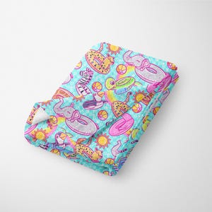 May include: A turquoise blue throw blanket with a repeating pattern of various animals riding inflatable pool floats. The animals include a zebra, a cheetah, a turtle, a penguin, and an elephant. The floats are in various colors, including pink, yellow, and blue. The background is a light blue with white polka dots.