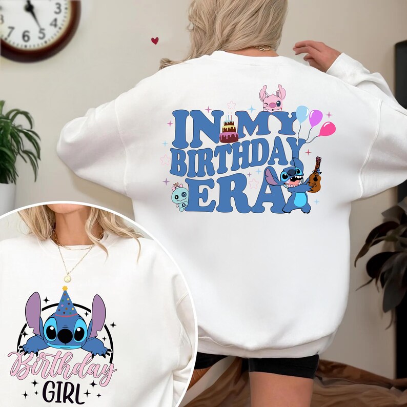 A person wearing a white sweatshirt with a birthday-themed design, including a character and text.