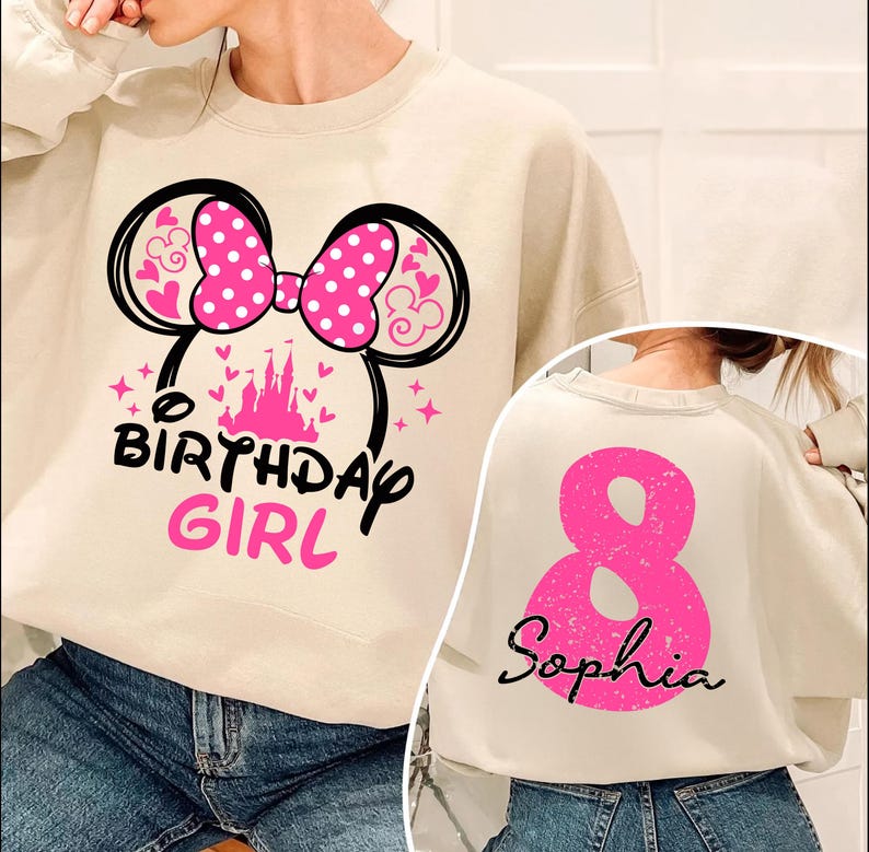 A person wearing a white sweatshirt with a pink and black design, including a large pink number 8 and a Minnie Mouse-inspired bow. The sweatshirt also has the text "BIRTHDAY GIRL" printed on it.