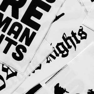 May include: Close-up of several white stickers with black text. The stickers are layered on top of each other. The text on the stickers reads "Human Rights" and "What's More Important".