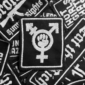 May include: A black and white embroidered patch with a fist in a circle, a transgender symbol, and the text "Fight for Rights".
