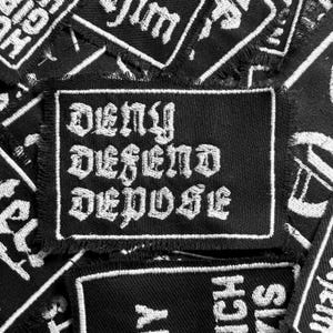 May include: Black and white embroidered patch with the words "Deny Defend Depose" in a gothic font.