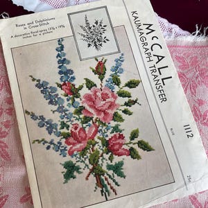 May include: Vintage McCall Kaumagraph Transfer pattern for cross-stitch, featuring a floral spray of roses and delphiniums. The design is in shades of pink, blue, and green, with the text "Roses and Delphiniums in Cross-Stitch" and "A decorative floral spray 13 1/8 x 18 5/8 inches for a picture".
