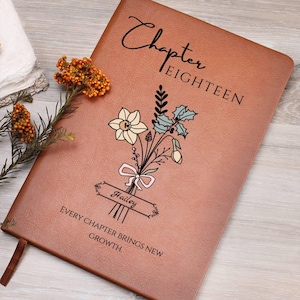 Pode incluir: Um diário de couro castanho com as palavras "Chapter EIGHTEEN" e "Every Chapter Brings New Growth" impressas na capa. Uma ilustração de buquê floral e o nome "Hailey" também estão presentes. Uma fita de marcador castanha é visível.