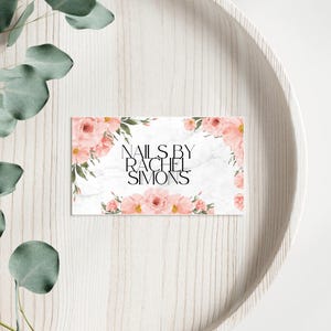 Könnte beinhalten: Eine weiße Visitenkarte mit Marmorhintergrund und rosafarbenem Blumendesign. Der Text "Nails by Rachel Simons" ist in Schwarz gedruckt.