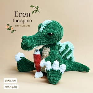 Puede incluir: Un juguete de dinosaurio Spinosaurus de ganchillo verde hecho a mano con vientre y detalles blancos. El dinosaurio sostiene un pez rojo y blanco. El texto "Eren the spino PDF PATTERN" se muestra en la imagen.