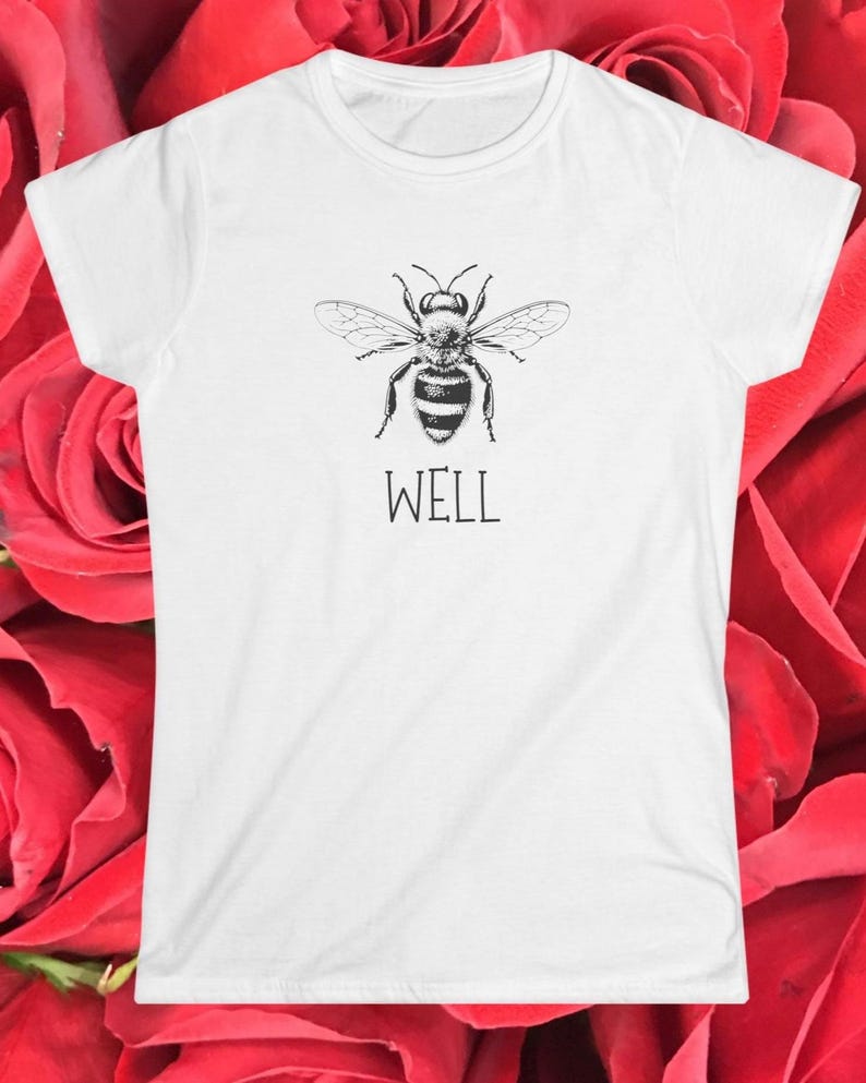 Op de afbeelding: Wit T-shirt met een zwart-witte illustratie van een bij. Onder de bij staat het woord "WELL" in een strak lettertype. De tee heeft een ronde hals en korte mouwen.