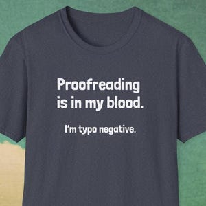 Pu&ograve; includere: T-shirt blu navy con testo bianco: "Proofreading is in my blood. I'm typo negative." La maglietta ha girocollo e maniche corte. Lo sfondo &egrave; verde.