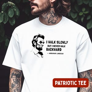 May include: White t-shirt featuring a black and white portrait of Abraham Lincoln with the quote "I walk slowly but I never walk backward." The words "PATRIOTIC TEE" are printed in red on the bottom.