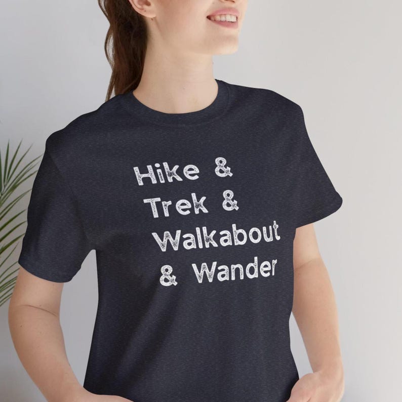 K&ouml;nnte beinhalten: Dunkelblaues T-Shirt mit den wei&szlig;en Worten "Hike & Trek & Walkabout & Wander" in verblichener Schrift. Das T-Shirt hat einen Rundhalsausschnitt und scheint aus einem weichen Material zu sein. Es ist ein Freizeitkleidungsst&uuml;ck.