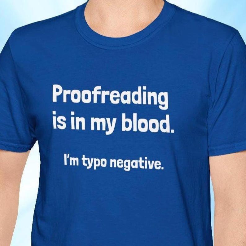 Pu&ograve; includere: T-shirt blu reale con testo bianco: "Proofreading is in my blood. I'm typo negative." La maglietta, a girocollo, sembra essere realizzata in un materiale morbido.
