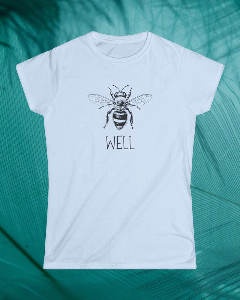 Op de afbeelding: Wit t-shirt met een zwart-witte illustratie van een gedetailleerde bij. Onder de bij staat het woord "WELL". Het t-shirt heeft een ronde hals en korte mouwen. De afbeelding toont het ontwerp van de bij.
