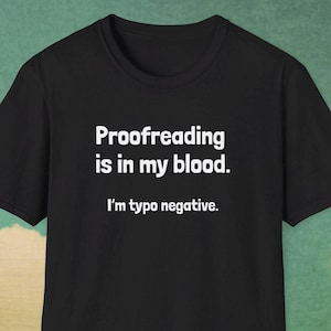 Peut inclure: T-shirt noir avec texte blanc : "Proofreading is in my blood. I'm typo negative." Le t-shirt à manches courtes a un col rond. Le texte est centré sur le devant du vêtement.