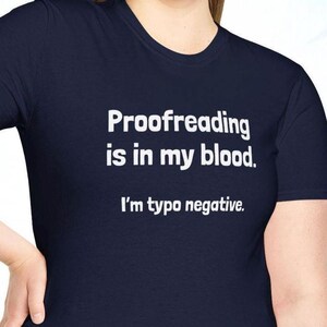 Pu&ograve; includere: T-shirt blu navy con la scritta bianca: "Proofreading is in my blood. I'm typo negative." La maglietta ha un girocollo e maniche corte. Il testo &egrave; in grassetto.