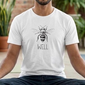 Op de afbeelding: Wit t-shirt met een zwart-witte bijenillustratie en het woord 'WELL' eronder. Het t-shirt is gemaakt van een zacht materiaal en is geschikt voor dagelijks gebruik. Het ontwerp is eenvoudig en opvallend.